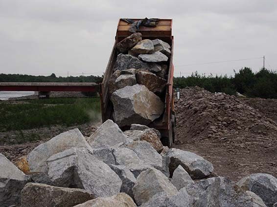 Camión tolva descargando roca clasificada para la construcción de un enrocado fluvial
